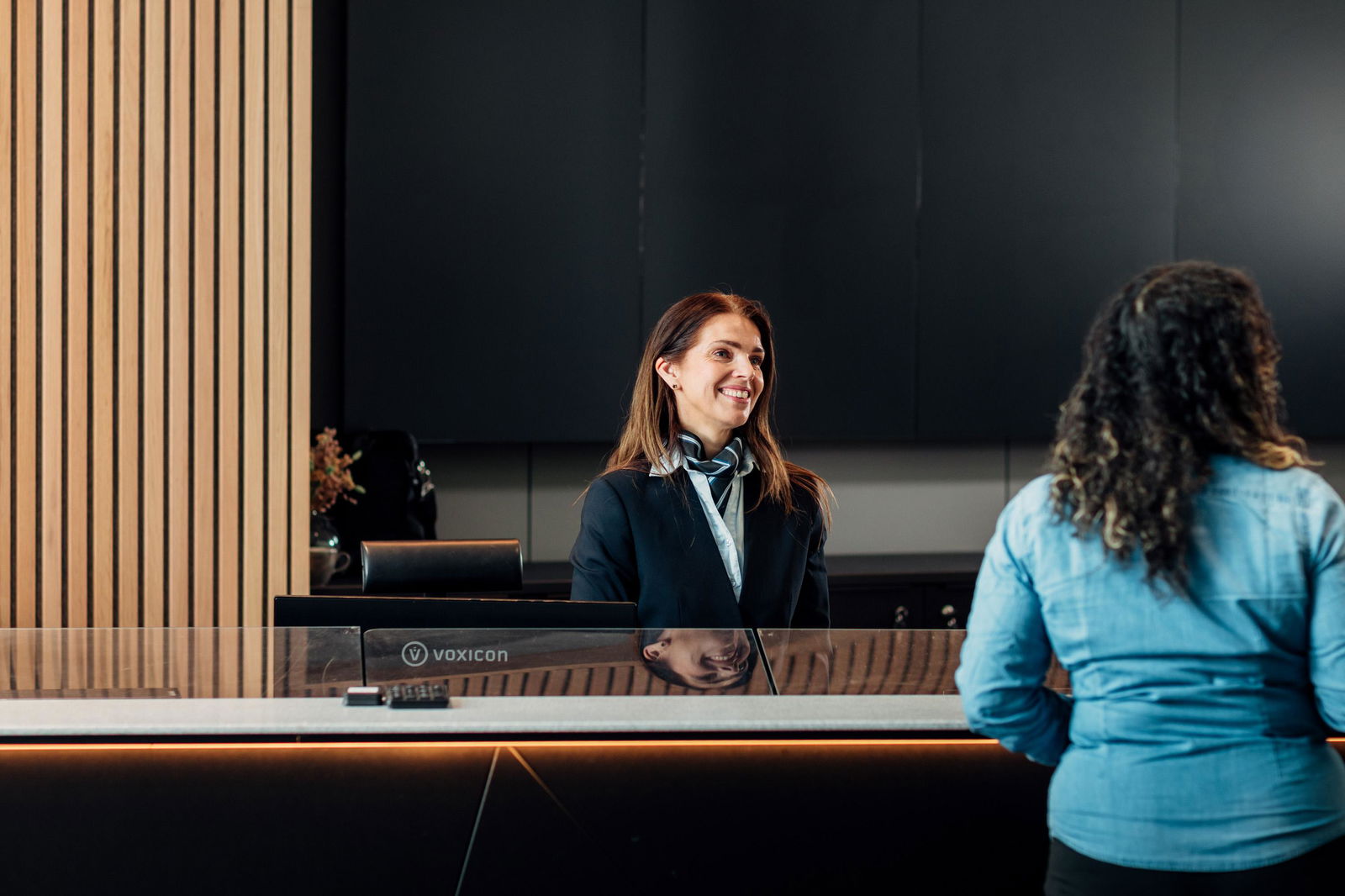 Resepsjonist i resepsjon, smiler til kunde