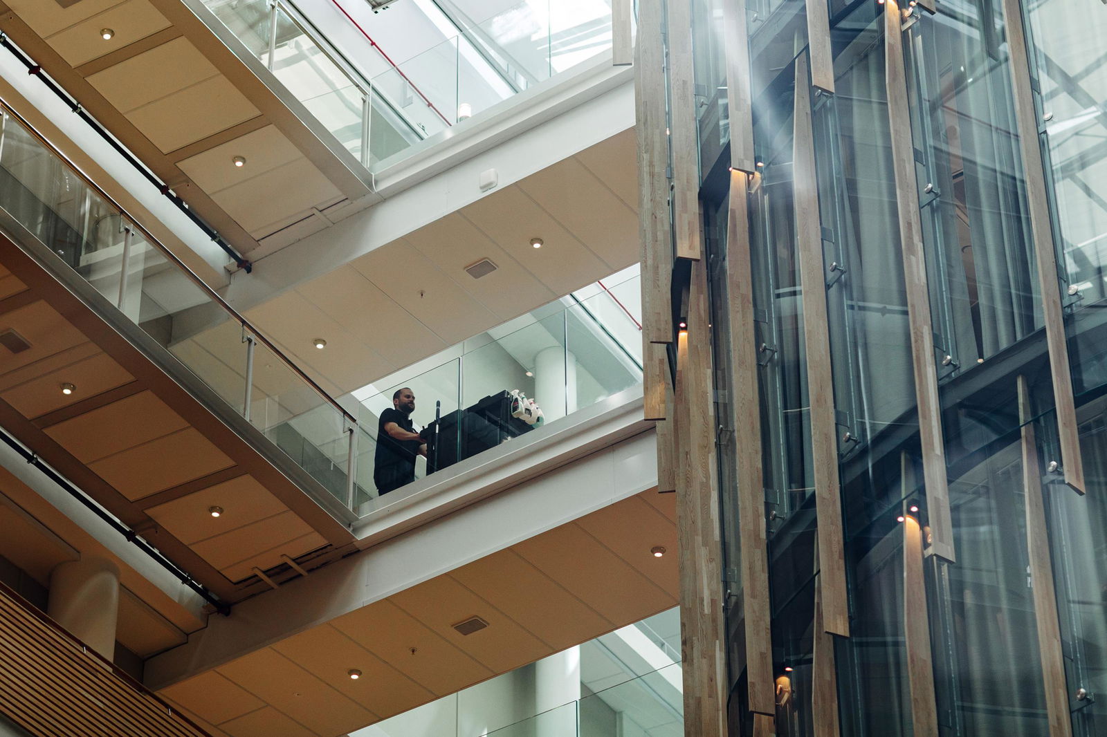 Renholder med tralle, sett nedenfra mens han går over en bro inne i et bygg