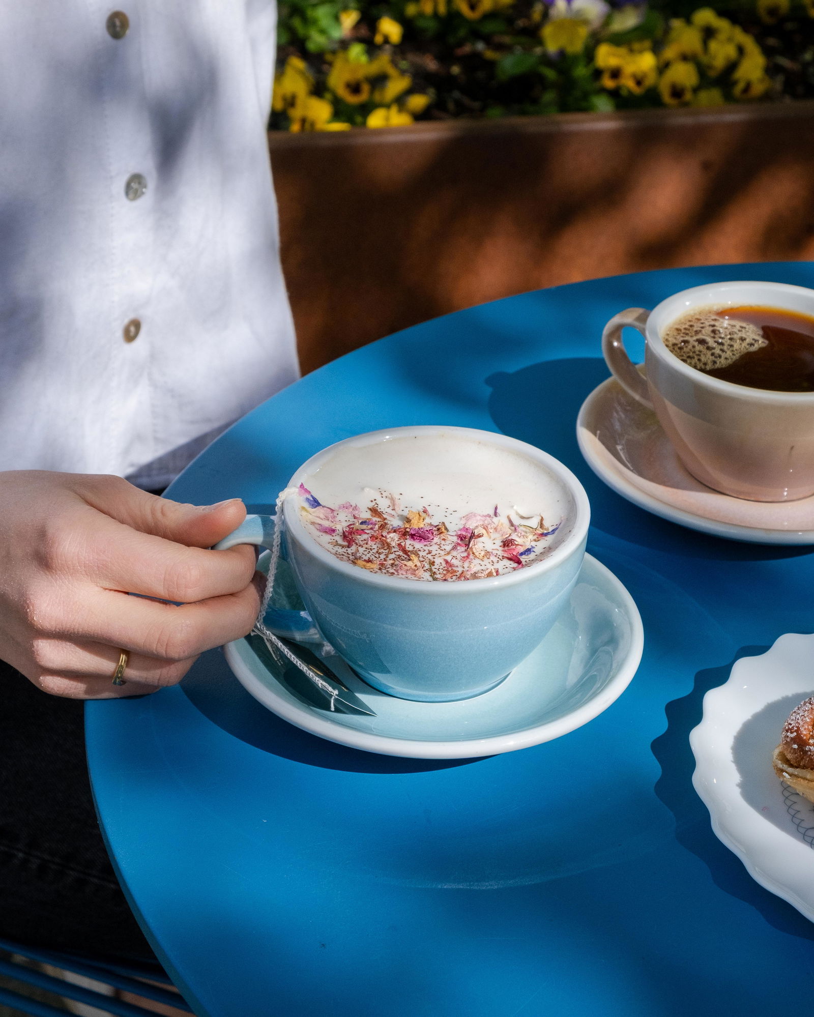 Teacup on blue table, a woman's hand holds the handle. Outdoors.