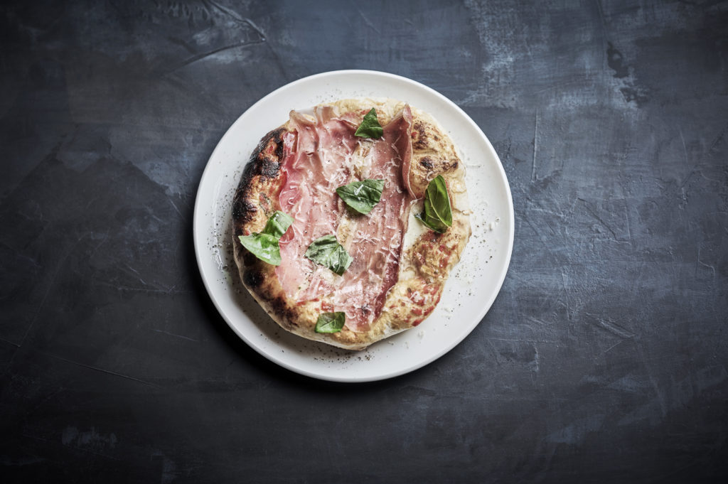 pizza med spekeskinke og basilikum på tallerken, sett ovenfra